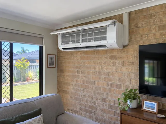 Open split-system air conditioner on a brick wall with clean filters visible in a living room in Pimpama