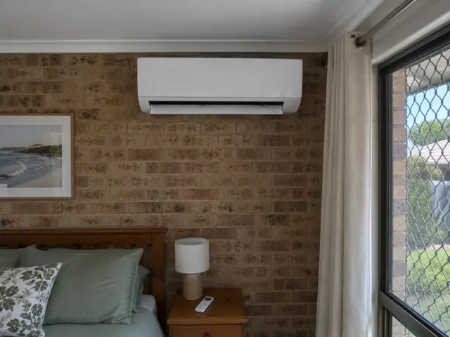 Split system mounted on a brick bedroom wall above a bed with louvre open in Coomera