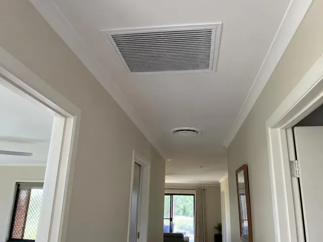 Ceiling return-air grille and round outlet in a narrow hallway with white trim in Ormeau