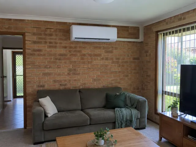 Wall-mounted split system on a brick living room wall above a sofa in a home in Coomera